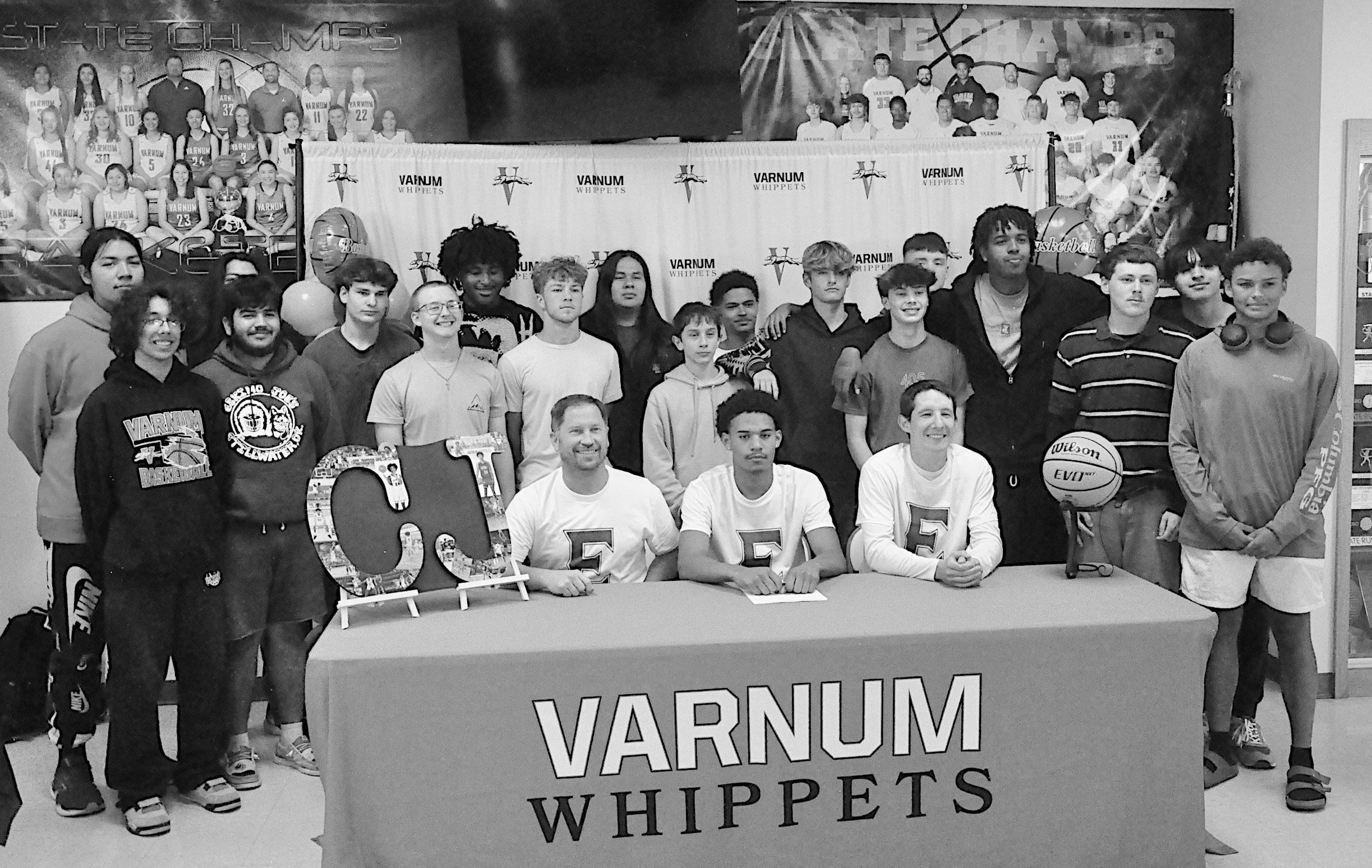 Varnum Whippet C.J. Benard signs his letter of intent to play for Eastern Oklahoma State College Monday. Pictured is Benard with Coaches and the Varnum basketball team. Staff Photo by Bill Anderson