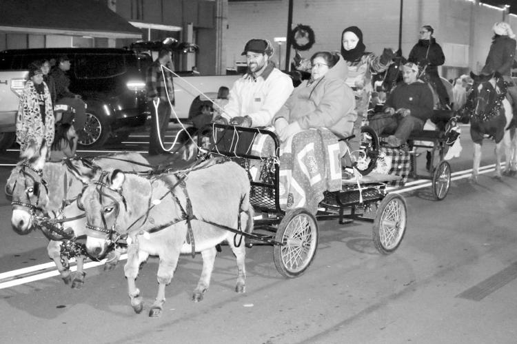 Representatives of Sealock Farms ride in a wagon pulled by a team of donkeys in Saturday evening’s Christmas parade. The event featured multiple entries, including floats, dancers, a marching band and more. The cool weather didn’t deter spectators, as