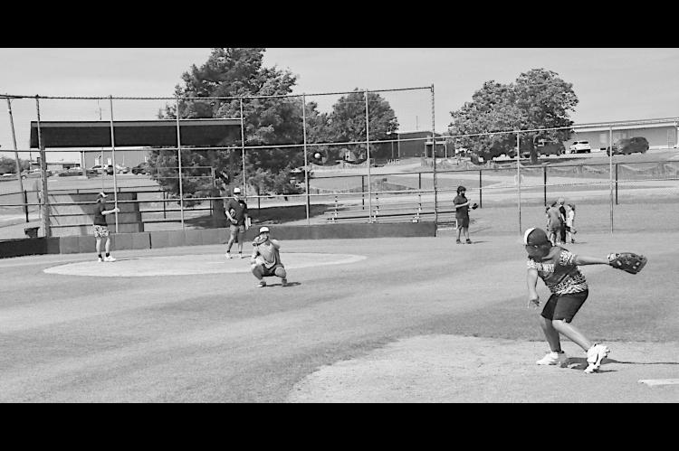 The Varnum coaching staff help the kids in the catcher’s position Monday. Kids rotated positions throughout the day. Staff Photo by Bill Anderson