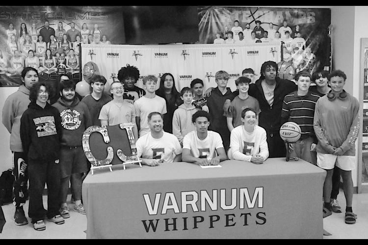 Varnum Whippet C.J. Benard signs his letter of intent to play for Eastern Oklahoma State College Monday. Pictured is Benard with Coaches and the Varnum basketball team. Staff Photo by Bill Anderson