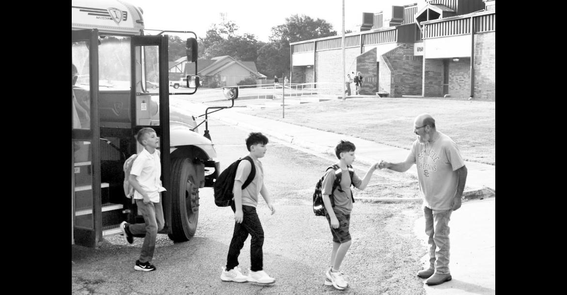 Northwood teacher Mitch Wainright stands ready to “bump knucks” with students Benjamin Norman, Conner Norman and Isiah McGee as they get off the bus for the first day of classes on Thursday, Aug. 6. —Staff Photo by Andy Wilson