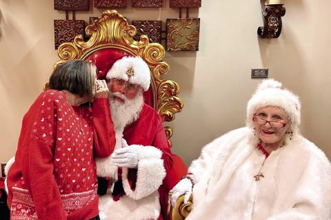 Seminole resident Carolyn Green sits on Santa’s knee and whispers her Christmas wishes to him in the lobby of the McSwain Theatre in Ada Friday night, Dec. 19. Mr. and Mrs. Claus passed out plenty of yuletide cheer to the theatre’s patrons. —Staff P